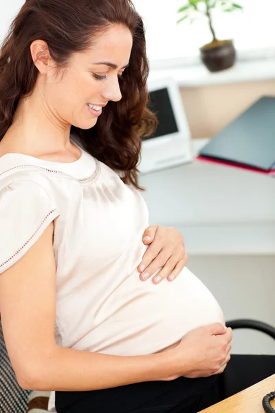 Embarazada mujer de negocios tocando su vientre sentada en su escritorio —  Fotos de Stock