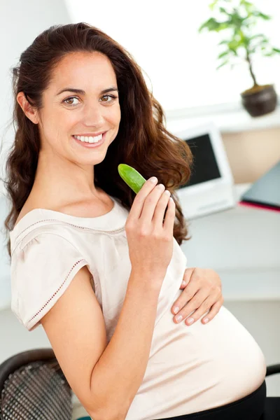 Bright pregnant woman eating a gherkin in her office — Stock Photo, Image