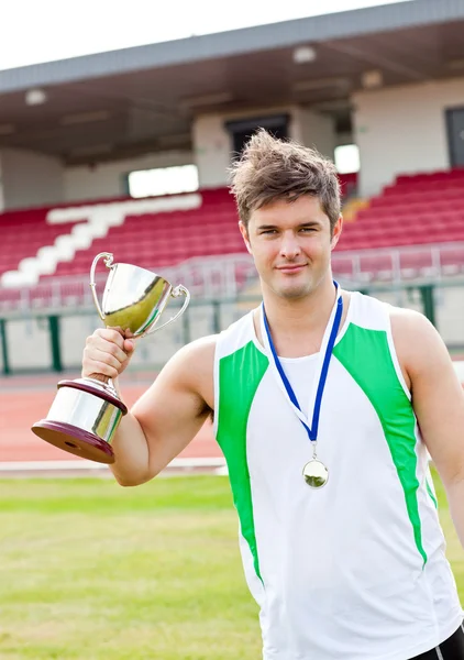 Delighted male athlete holding a cup and a medal standing — Stock Photo, Image