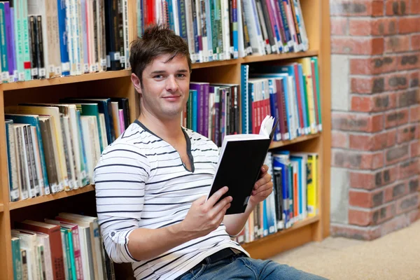 Guapo estudiante masculino leyendo un libro sentado en el suelo —  Fotos de Stock