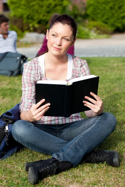Яскрава студентка читає книгу, що сидить на траві — стокове фото