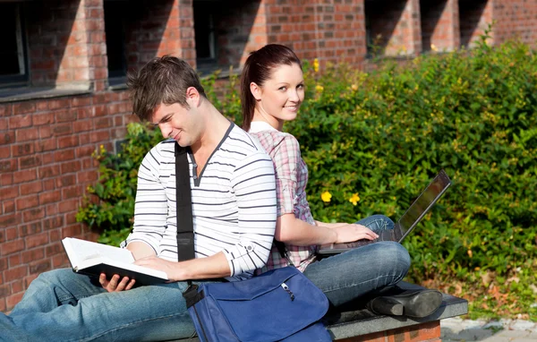 Το υπέροχο ζευγάρι των μαθητών, χρησιμοποιώντας ένα φορητό υπολογιστή και διαβάζοντας ένα βιβλίο — Φωτογραφία Αρχείου