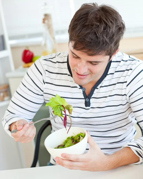 Delighted young man eating a healthy salad in the kitchen — Stock Photo, Image