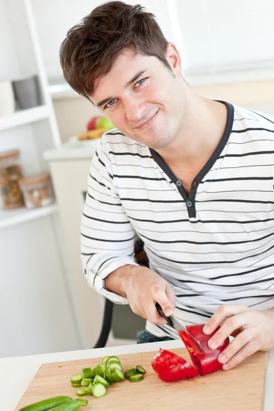Jeune homme souriant coupant des légumes dans la cuisine — Photo