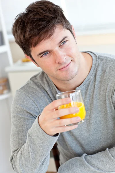 Привлекательный молодой человек, пьющий апельсиновый сок на кухне — стоковое фото
