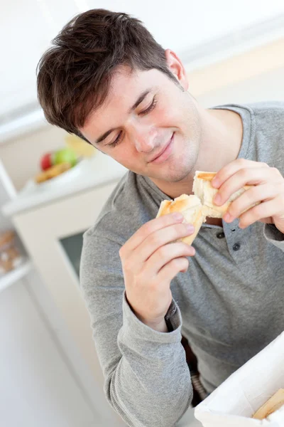 Delighted man eating bread in the kitchen — Stock Photo, Image