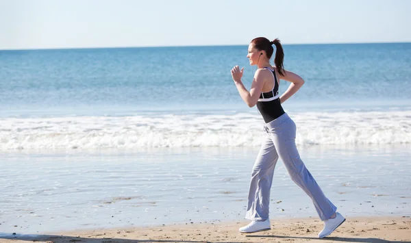 Sportliche Frau läuft am Strand und hört Musik — Stockfoto