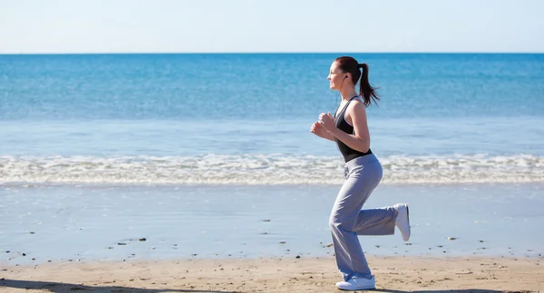 Sporty woman running on the beach and listening to music — Stock Photo, Image