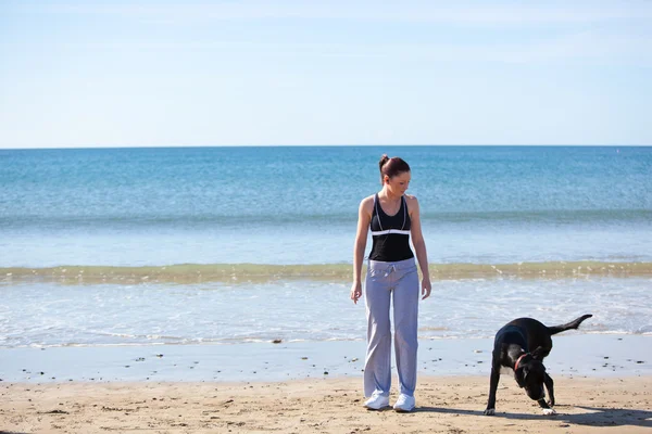 Молодая спортивная женщина с собакой на пляже — стоковое фото