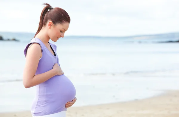 Беременная женщина трогает живот на пляже. — стоковое фото