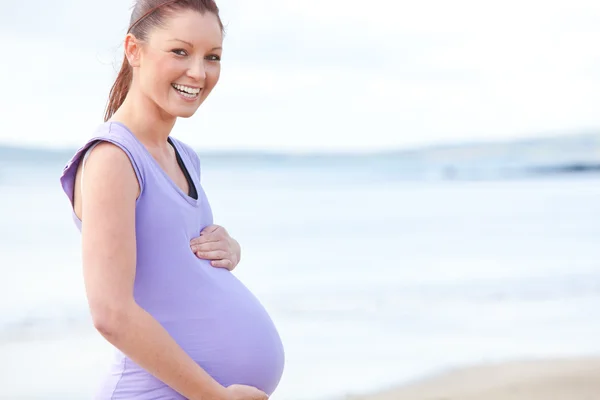 Usmívající se těhotná žena stojící na pláži — Stock fotografie