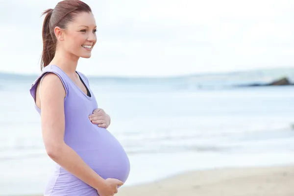 Улыбающаяся беременная женщина, стоящая на пляже — стоковое фото