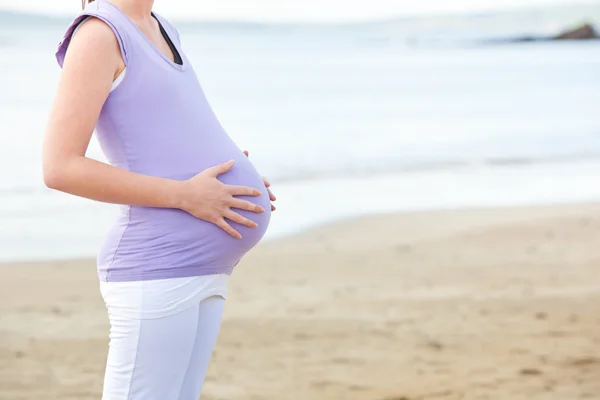 Primer plano de una mujer embarazada parada en la playa — Foto de Stock