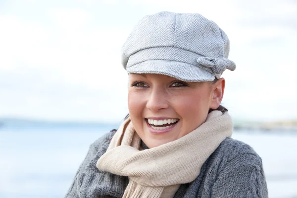 Смеющаяся белая женщина в шапке и шарфе стоит на пляже — стоковое фото