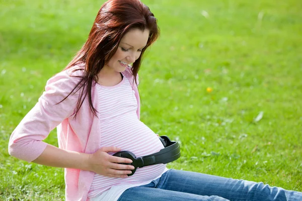 彼女の腹で、ヘッドフォンとうれしそうな妊娠中の女性 — ストック写真