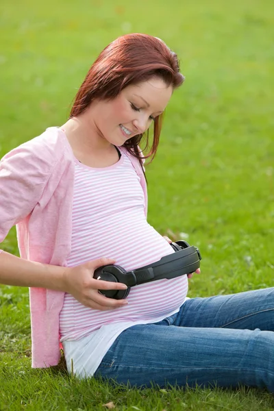 彼女の腹で、ヘッドフォンとうれしそうな妊娠中の女性 — ストック写真