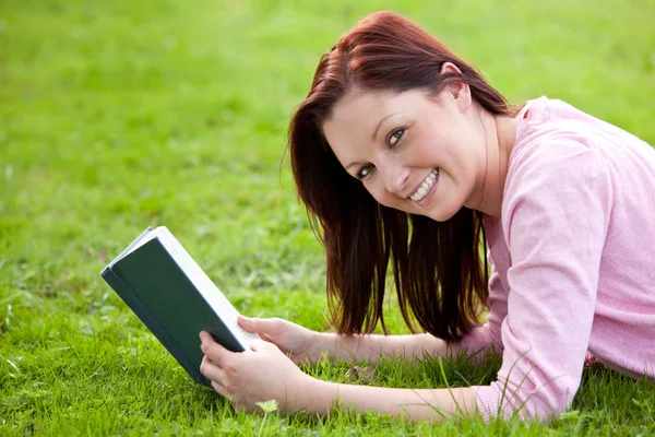 Jovem alegre lendo um livro deitado na grama — Fotografia de Stock