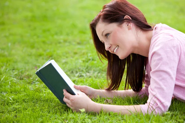 Veselá mladá žena s knihou, ležící na trávě — Stock fotografie