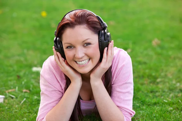 Delighted young woman listening to music with headphones lying on the grass — Stock Photo, Image