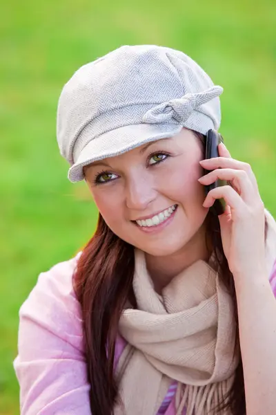 Красивая молодая женщина в шапке и шарфе разговаривает по телефону на траве — стоковое фото