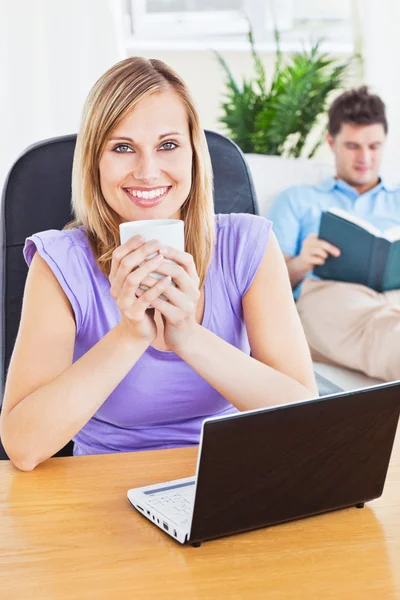 Schöne Frau trinkt Kaffee und benutzt Laptop, während Freund — Stockfoto
