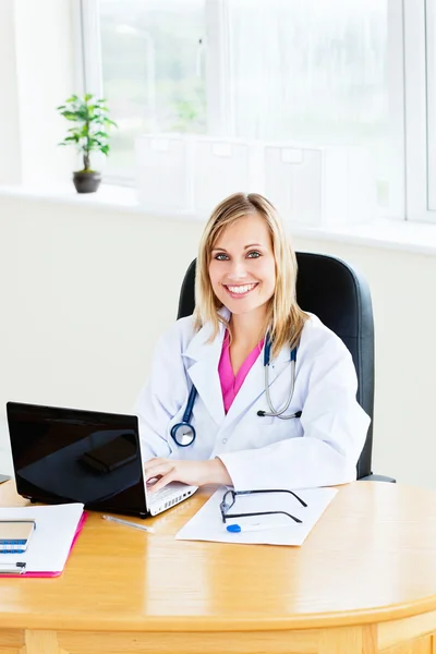 Blond vrouwelijke arts zitten in haar kantoor werken op een laptop — Stockfoto