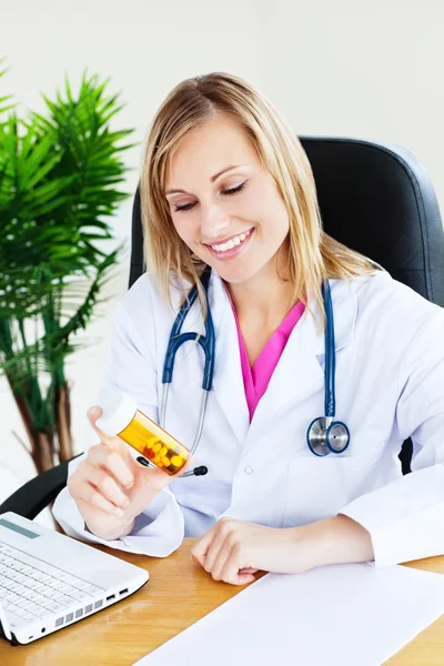 Médica feminina brilhante com estetoscópio olhando para pílulas — Fotografia de Stock