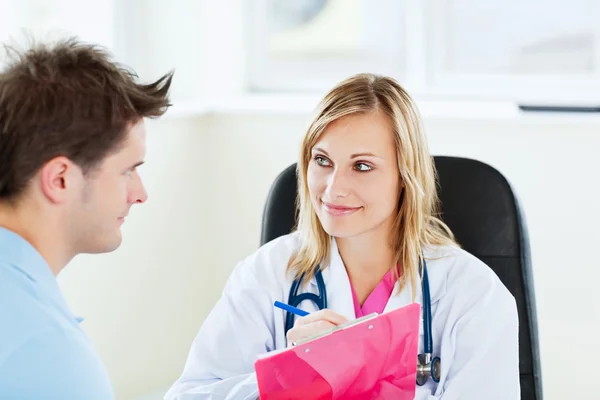 Médico sonriente escribiendo prescripción durante una cita con un —  Fotos de Stock