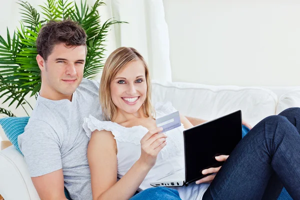 Pareja joven con ordenador portátil y tarjeta de crédito bying en línea acostado en t — Foto de Stock