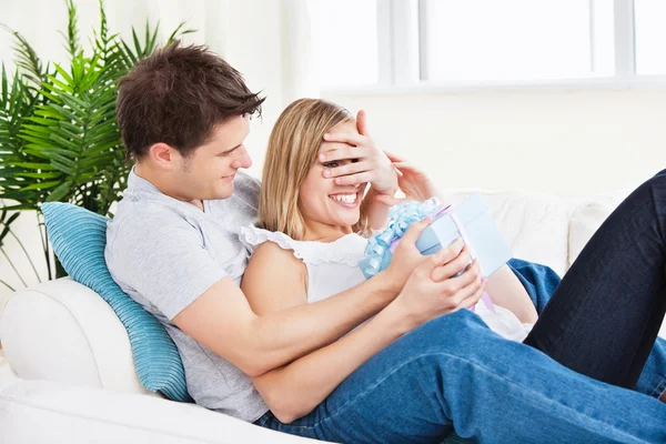 Young couple lying on the sofa with a present — Stock Photo, Image