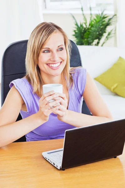 Mulher sorridente segurando um copo de água atrás de seu laptop — Fotografia de Stock