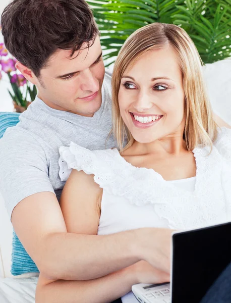快乐的年轻夫妇坐在一张沙发使用的便携式计算机上的肖像 — 图库照片