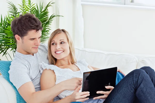 微笑着坐在沙发上使用 lapto 的年轻夫妇的肖像 — 图库照片