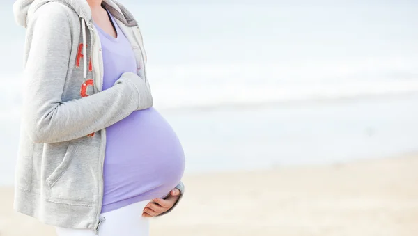 Mujer joven embarazada caminando por la playa — Foto de Stock