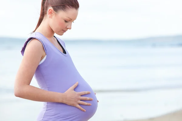 Беременная красивая женщина наблюдает за своим желудком на пляже — стоковое фото
