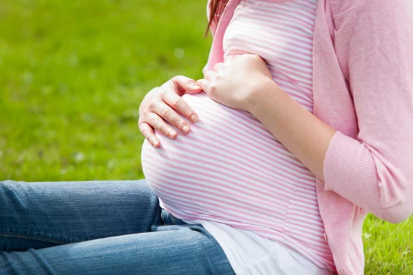 Zwangere jonge vrouw zittend op het gras — Stockfoto