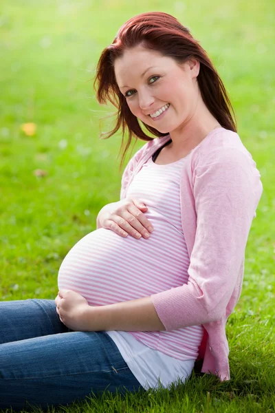 Fajna młoda kobieta w ciąży, siedząc na trawie — Zdjęcie stockowe