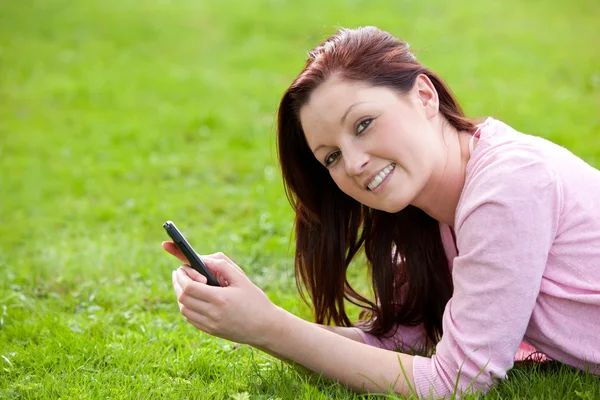 Atractiva joven embarazada acostada en el césped mensajes de texto —  Fotos de Stock