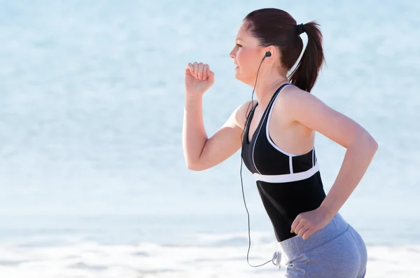 Mujer joven corriendo en la playa escuchando música — Foto de Stock