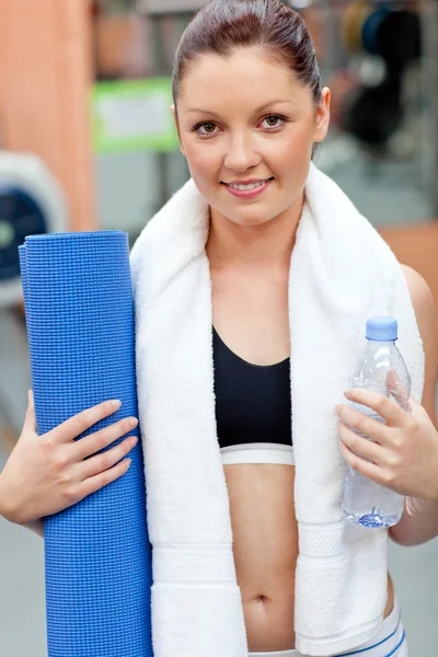 Спортивная женщина с бутылкой воды и ковриком для упражнений, смотрящая на — стоковое фото