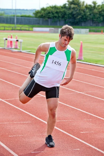 Knappe sprinter streching voordat een race staande in een stadion — Stockfoto