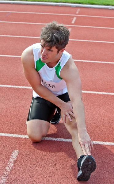 Jovem masculino sprinter streching no chão antes de uma corrida em um st — Fotografia de Stock