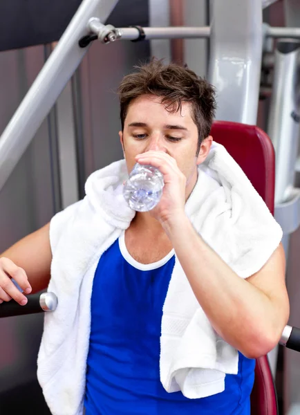 Атлетик пьет во время упражнений, сидя на скамейке прессы — стоковое фото
