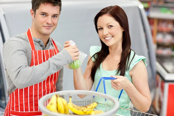 Vendedor en un supermercado dando manzanas a su hembra sonriente — Foto de Stock