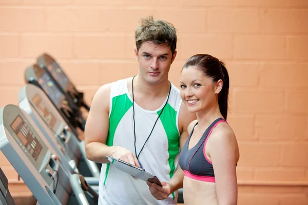 Hübsche Frau auf einem Laufband mit ihrem Trainer, der Ergebnisse zeigt — Stockfoto