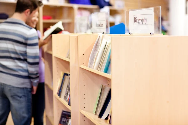 Close-up of a bookshelves in a library with students reading boo — Stock Photo, Image