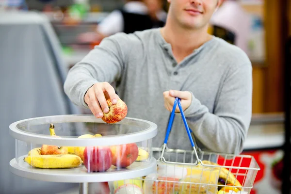 Close-up of a young man putting apples in his shopping basket — Stock Photo, Image