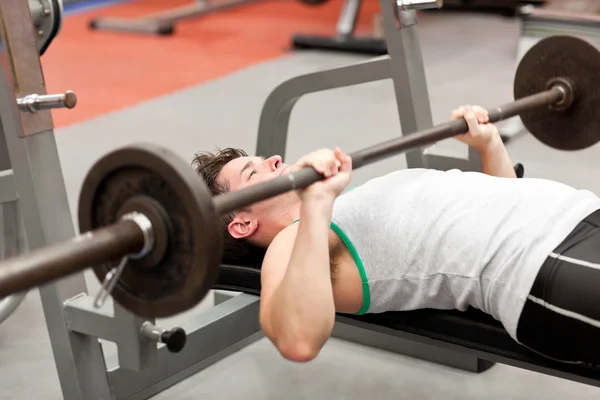 Musculoso joven usando levantamiento de pesas tumbado en un gimnasio —  Fotos de Stock