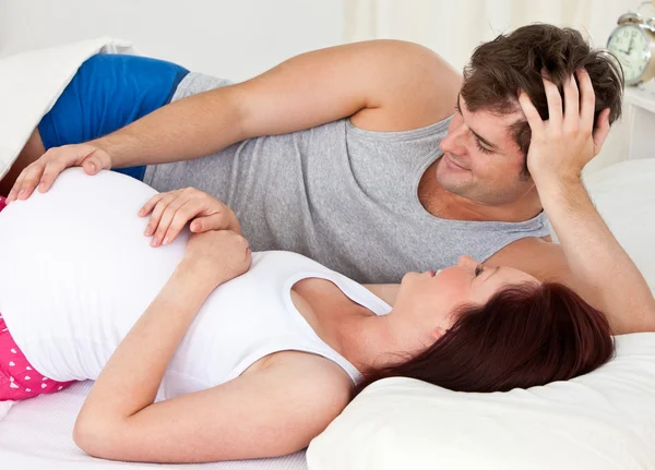 Niedlicher Mann berührt den Bauch seiner schwangeren Frau, die auf dem Bett liegt — Stockfoto