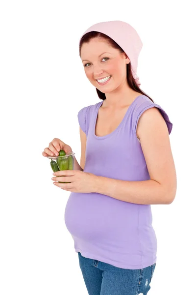 Linda futura mamá sosteniendo pepinillos en un vaso sonriendo al camer — Foto de Stock
